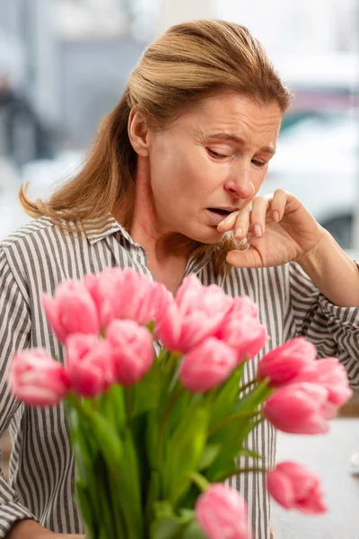 Housewife wearing striped shirt sneezing after receiving bouquet — Stock Photo, Image