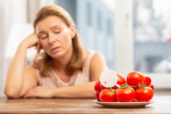 Ama de casa sentada en la mesa y mirando los tomates pero con alergia — Foto de Stock