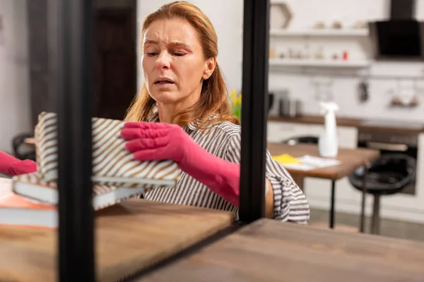 Mature blond wife feeling not good while dusting the shelves — Stock Photo, Image
