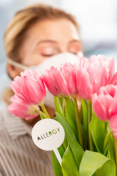 Mujer de pelo rubio que tiene alergia estacional oliendo tulipanes rosados — Foto de Stock