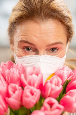 Maske takıyor ve Pembe Lale tutan olgun hoş kadın