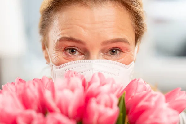 Kobieta czuje się spełniony po zapachu tulipany, ale w masce — Zdjęcie stockowe