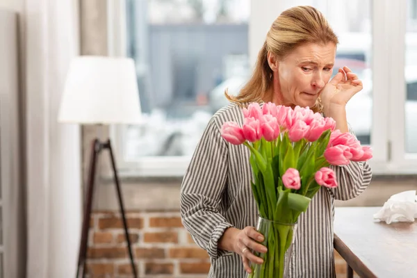 Mujer rubia sosteniendo jarrón con tulipanes rosados sintiendo alergia —  Fotos de Stock