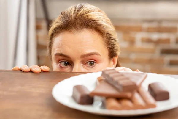 Grünäugige reife Frau versteckt sich und betrachtet dunkle Schokolade — Stockfoto