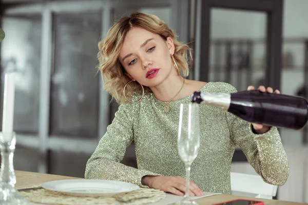 Blonde-haired curly woman pouring champagne into glass