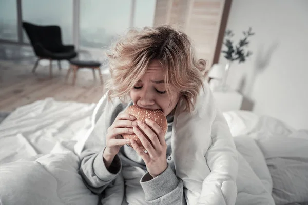 Mujer mordiendo hamburguesa mientras come demasiado en la depresión —  Fotos de Stock