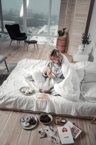 Vista superior de la mujer sentada en su cama rodeada de comida — Foto de Stock