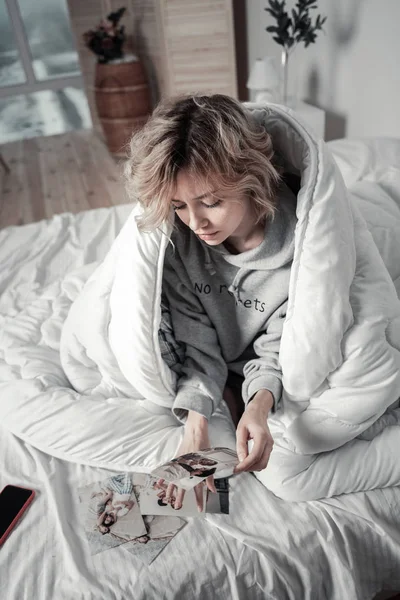 Кучерява блондинка сидить у ліжку і дивиться на фотографії з колишнім — стокове фото