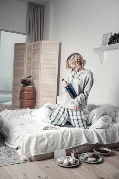 Mujer joven bebiendo champán y bailando en la cama después de la ruptura — Foto de Stock