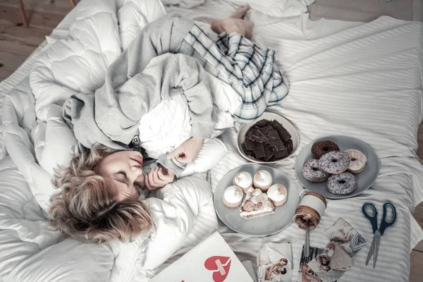 Mujer solitaria estresada tumbada en la cama cerca de dulces y fotos — Foto de Stock