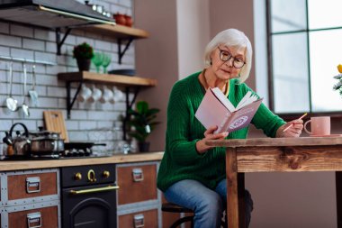 Smart white-haired lady in years making notes of vedic books clipart