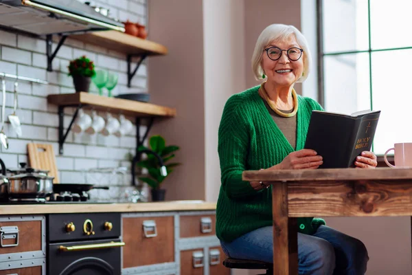 Lachende vrouw gelukkig houden boek in handen op keuken kamer — Stockfoto