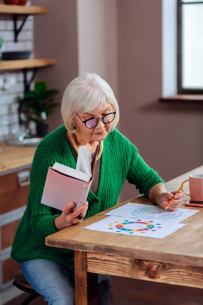 Пожилая женщина, работающая над пониманием ведических таблиц с помощью книги — стоковое фото