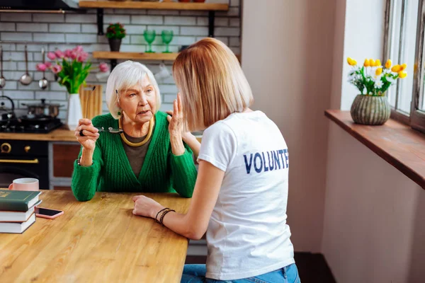 Nice-tilltalande socialarbetare som tröstar åldrande farmor i gröna ull kofta. — Stockfoto