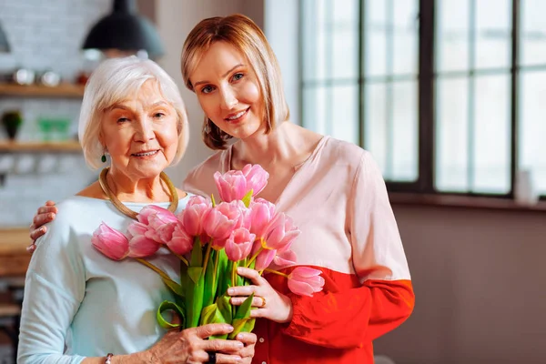 Прекрасная зрелая дочь дарит тюльпаны морщинистой седой матери — стоковое фото
