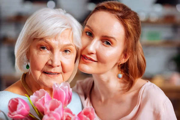 Portretfoto van volwassen dochter knuffelen grijs-haired moeder bedrijf tulpen — Stockfoto