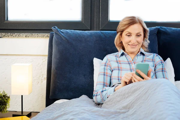 Mujer adulta concentrada apoyada en su cama y revisando las redes sociales — Foto de Stock
