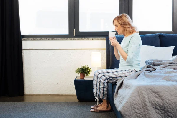 Agradable señora madura de pelo claro sentada en el borde de su cama — Foto de Stock