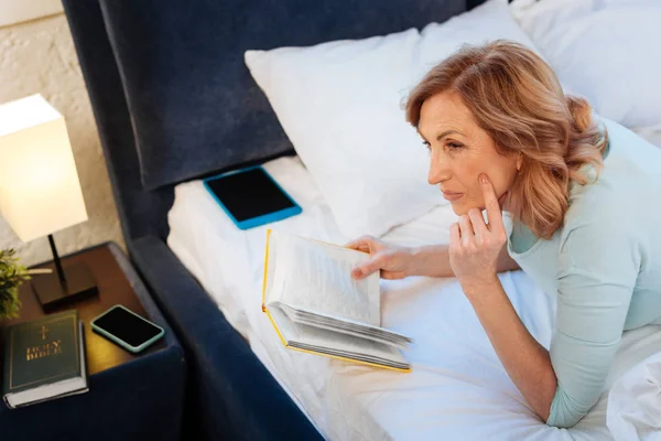 Preciosa mujer de pelo claro descansando en cama inacabada con libro de tapa dura — Foto de Stock