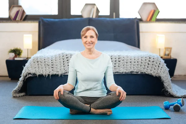 Mujer radiante agradable con amplia sonrisa teniendo entrenamiento de yoga en casa — Foto de Stock