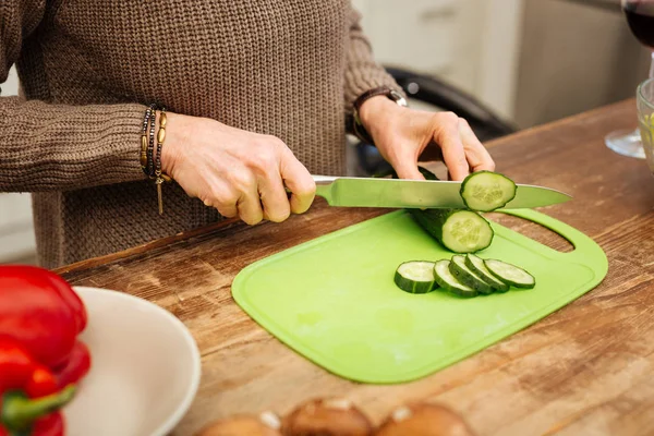 Attentive lady in warm sweater cutting cucumber while cooking — Stock Photo, Image