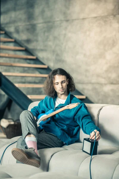 Long-haired extraordinary guy being alone at home and playing on guitar