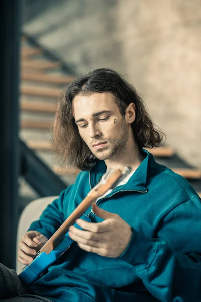 Unachtsamer, gutaussehender junger Mann, der Saiten auf seiner Gitarre tont — Stockfoto