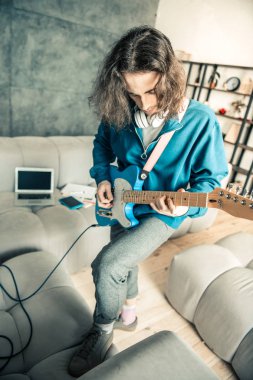 Yakışıklı müzisyen gri kanepeye ayak koyarak odaklı