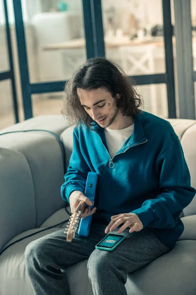 Jeune guitariste attentif aux cheveux longs tenant un instrument de musique — Photo