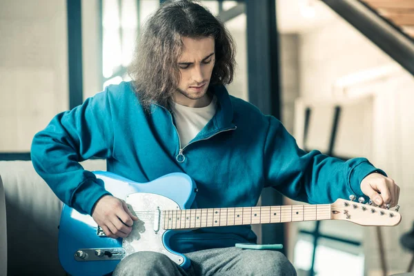 Geconcentreerde knappe ongebruikelijke man instellen op zijn elektronische gitaar snaren — Stockfoto