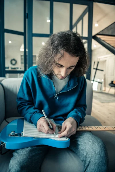 Homem de cabelos compridos concentrado colocando notebook em sua guitarra brilhante — Fotografia de Stock