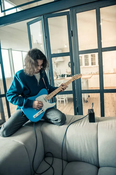 Músico de pelo largo enfocado que tiene su guitarra conectada al amplificador — Foto de Stock