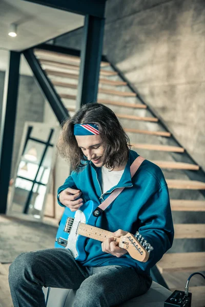 Sonriente chico de pelo largo siendo feliz mientras toca en la guitarra electrónica —  Fotos de Stock