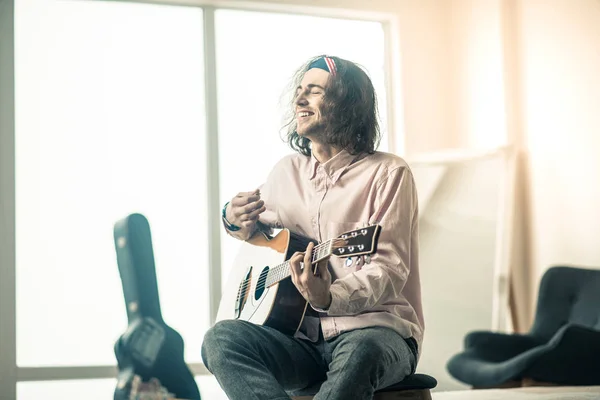 Alegre guapo joven guitarrista sentado en habitación luminosa — Foto de Stock