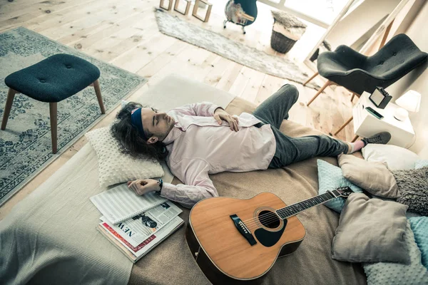 Achteloos dark-haired mannelijke musicus rust in de slaapkamer na herhaling — Stockfoto