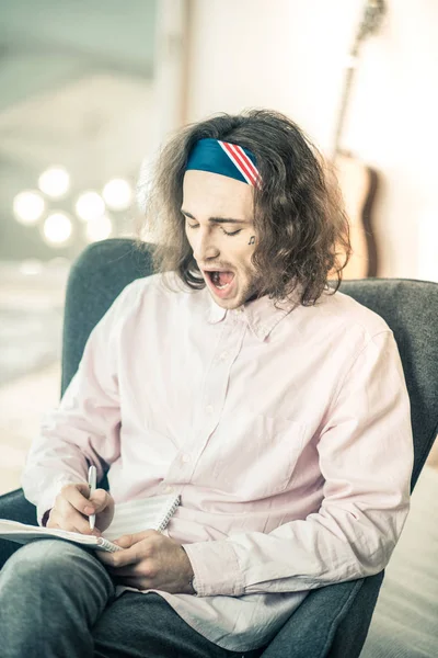 Tired long-haired talented man with tattoo on the face yawning — Stock Photo, Image