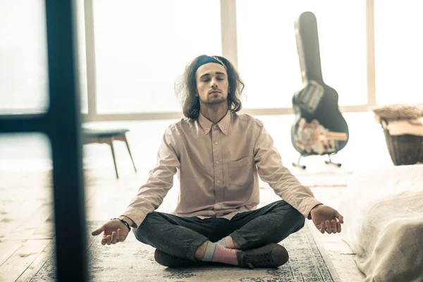 Peaceful long-haired man sitting in lotus posture in the middle of the room