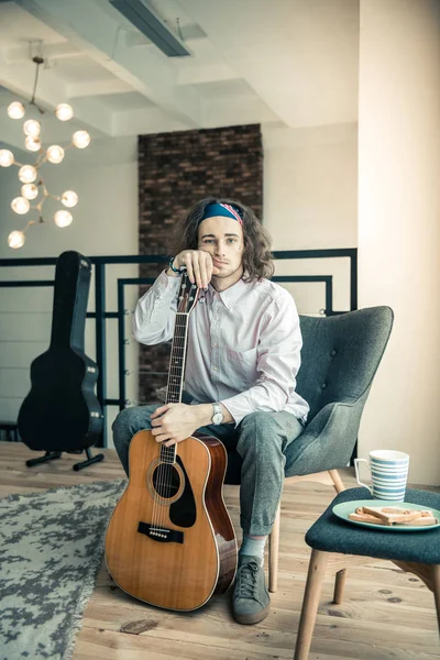 Cansado chico molesto con bandana colorido apoyándose en su guitarra —  Fotos de Stock