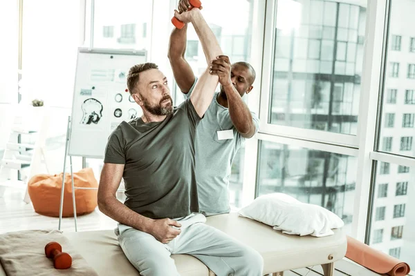 Zorgvuldige bebaarde mannelijke persoon tillen halter met hulp — Stockfoto