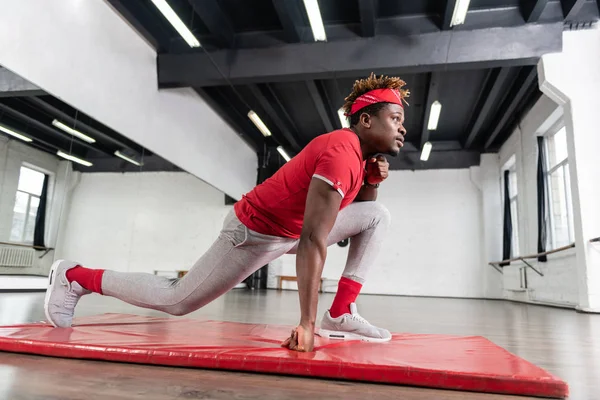 Focused in forma giovane ragazzo facendo squat larghi sul tappeto rosso — Foto Stock