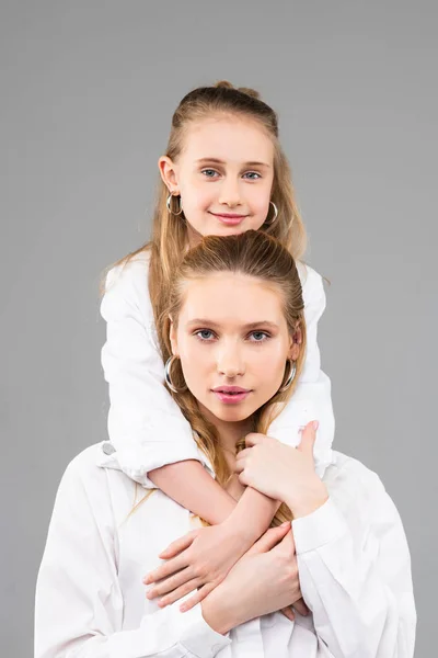 Sonriente y agradable niña con los ojos azules apoyados en su hermana mayor —  Fotos de Stock