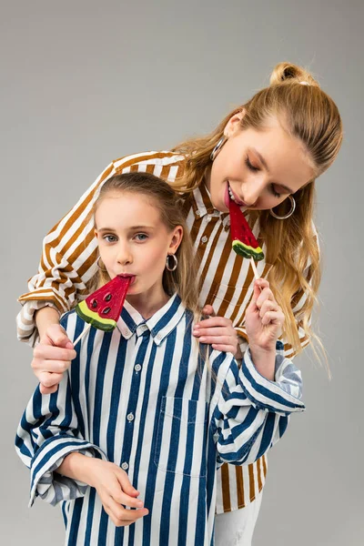 Mujer adulta sonriente de pelo largo proponiendo su caramelo de azúcar a su hermana pequeña — Foto de Stock