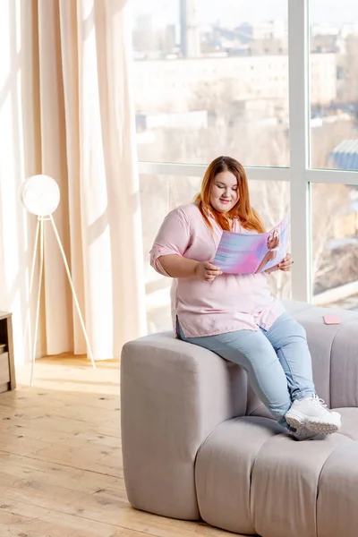 Positive plum woman reading about modern fashion trends