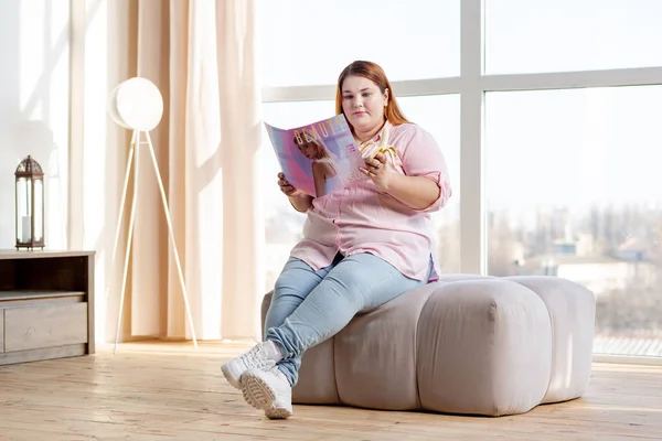 Приятная толстая женщина читает журнал дома — стоковое фото