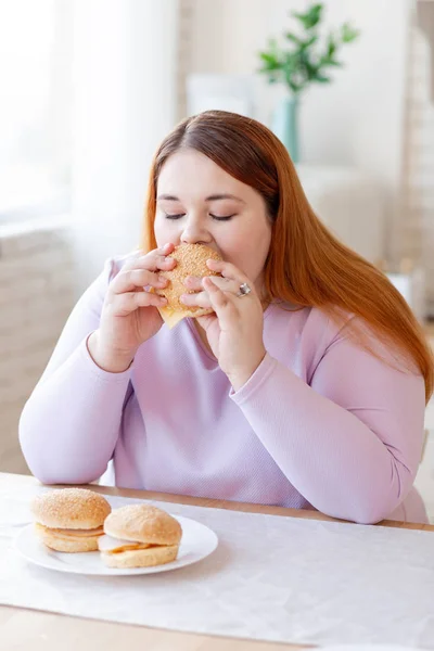 Mulher gorda agradável comer um hambúrguer saboroso — Fotografia de Stock