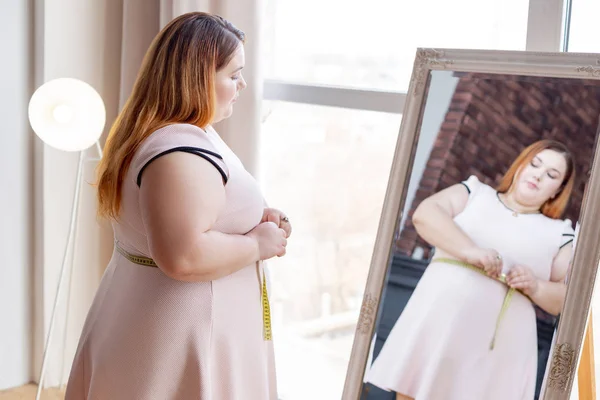 Приятная пухлая женщина смотрит в зеркало — стоковое фото