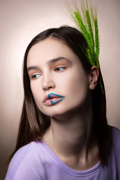 Appealing woman with blue lines on lips and green spikelet in hair