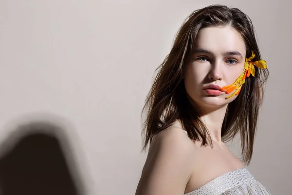 Model z grubą brwi stwarzające z pomarańczowym kwiatem we włosach — Zdjęcie stockowe