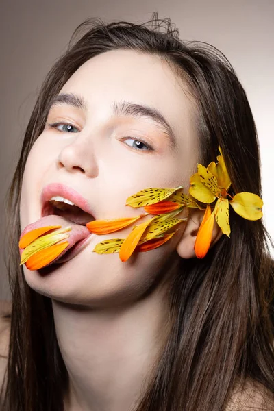 그녀의 혀에 꽃 꽃잎을가지고 있는 동안 포즈를 취한 블루 아이드 모델 — 스톡 사진