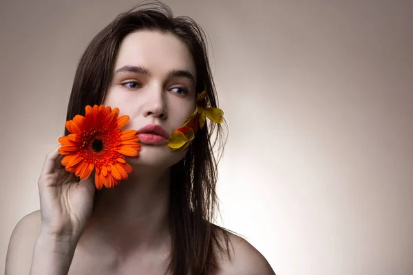 Modelo com algumas pétalas no rosto segurando flor de laranja — Fotografia de Stock